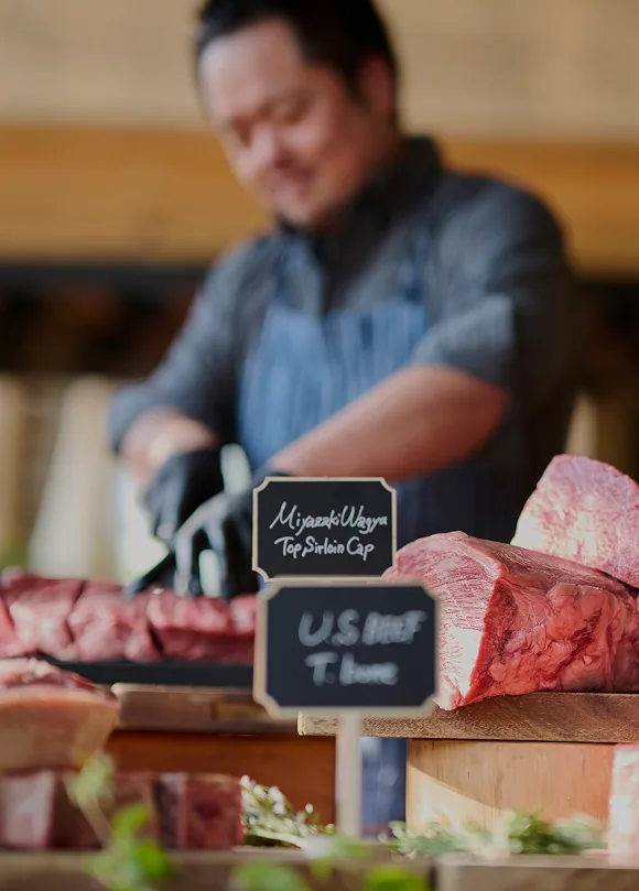 塊肉が並ぶカウンターで肉を切り分けるシェフ