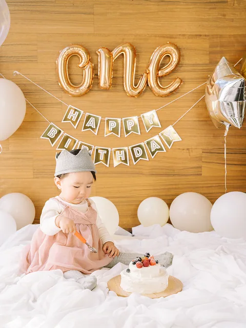 One のバルーンの前でスマッシュケーキを楽しむ1歳のお子様